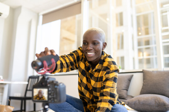 Smiling woman adjusting microphone while vlogging at home