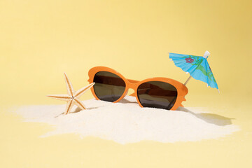 Sand island with orange sunglasses, umbrella and starfish on blue background, summer vacation concept.