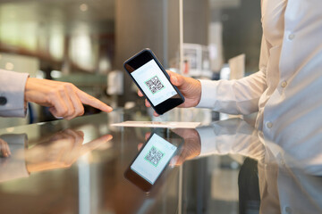 Female receptionist pointing at QR code scanned by male customer at desk