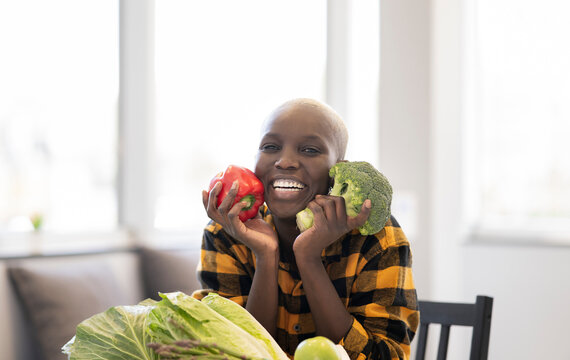 Smiling woman holding vegetables while sitting at home