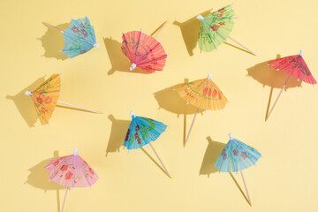 Multicolored cocktail umbrellas on yellow background in bright sunlight, summer party background.