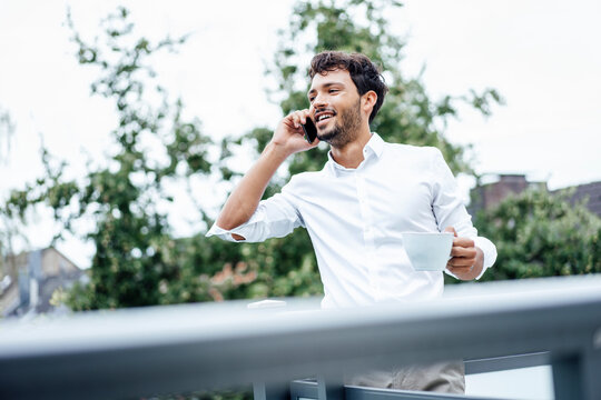 Smiling handsome man talking on smart phone while standing on balcony