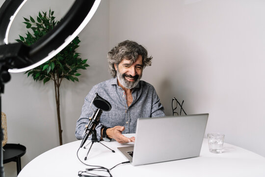 Senior male freelancer podcasting with laptop on table at home office
