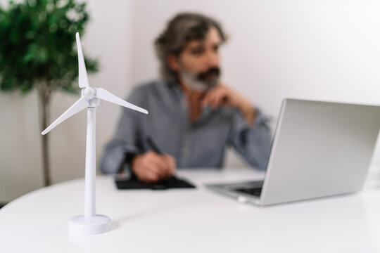 Wind turbine on table while businessman working in background at home office