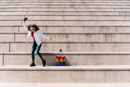 Young woman listening music through headphones and dancing on steps