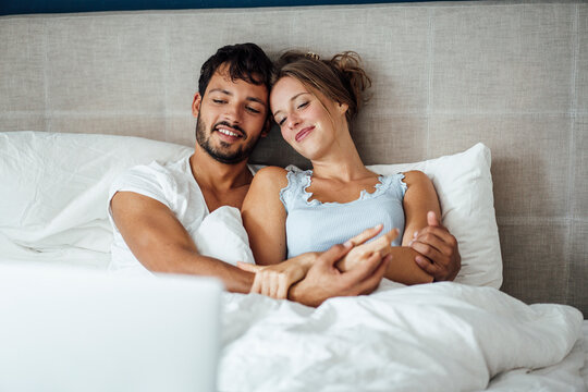 Young couple looking at laptop while sitting together on bed at home