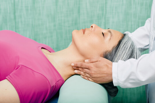 Woman patient lying on a massage table receives a therapeutic massage of neck and upper spine from osteopathic doctor