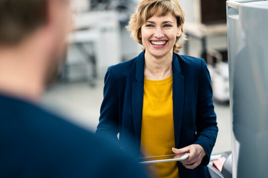 Smiling manager with digital tablet looking at colleague in workshop