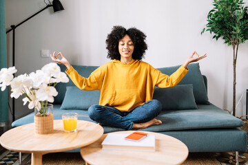 Young woman meditating while sitting on sofa at home