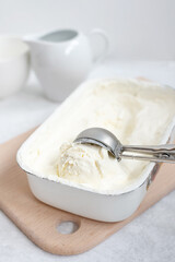 Homemade vanilla ice cream ball in spoon on ice cream container on white background, home cooking concept.