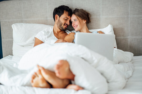 Smiling couple looking at each other while sitting on bed