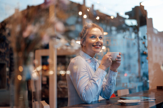 Thoughtful female entrepreneur with coffee cup smiling while looking through cafe window