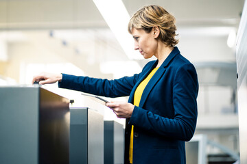 Female professional with digital tablet operating machine at printing factory