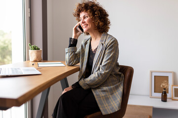 Female freelancer talking on smart phone while sitting on chair at home