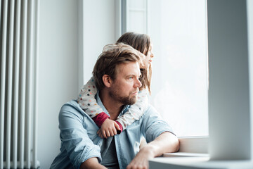 Girl with arm around of father looking through window at home