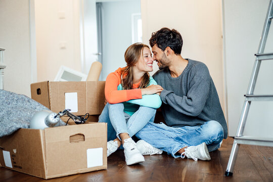 Smiling young couple sitting together by cardboard box at home