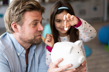 Daughter putting coin in piggy bank held by father at home