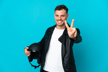 Caucasian man with a motorcycle helmet isolated on blue background smiling and showing victory sign