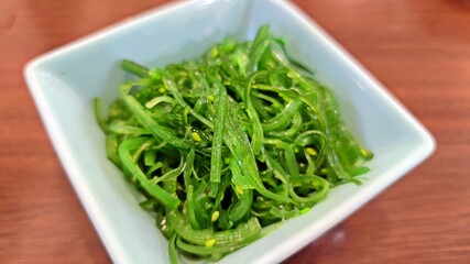 Chuka seaweed salad (Hiyashi Wakame), Seasoned seaweed in white square plate on wooden table. Japanese food. © Supratchai