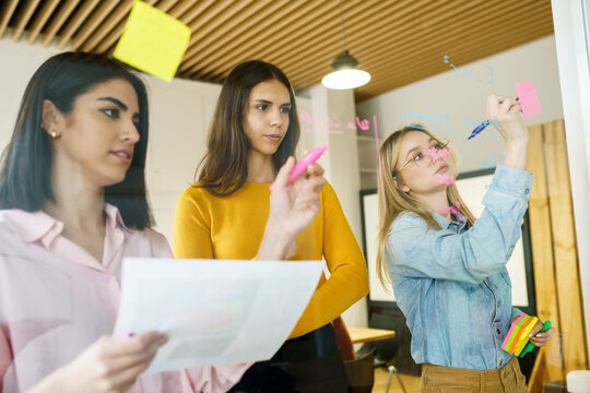Creative female professionals writing on glass in office
