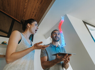 Physiotherapist and surprised female patient looking at holographic anatomical model of the spine