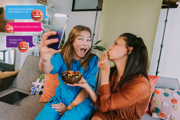 Female influencer filming with friend through mobile phone at home