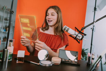 Teenage female influencer reading online feedback on futuristic digital tablet while podcasting at home