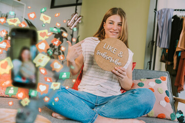 Female influencer showing like and subscribe cardboard while vlogging through mobile phone at home