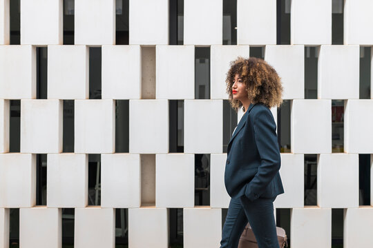 Afro female entrepreneur with hand in pocket walking by modern wall