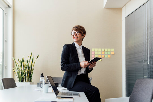 Thoughtful businesswoman holding digital tablet while sitting on desk in office