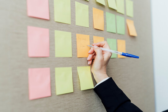 Female entrepreneur writing on adhesive notes sticked on beige wall