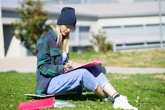 Young woman studying while sitting on skateboard in college campus during sunny day