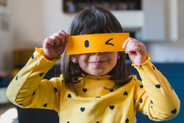 Girl holding yellow paper with winking emoticon at home