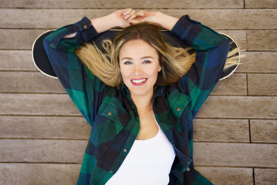 Smiling woman with arms raised lying on skateboard