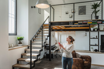 Young woman controlling smart home functions through mobile phone at modern home