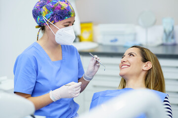 Female dentist wearing protective face mask holding dental equipments while talking with patient at clinic