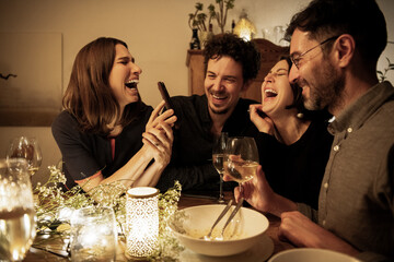 Male and female friends laughing while woman showing mobile phone at dining table