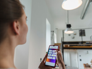 Young woman controlling light using mobile phone at home