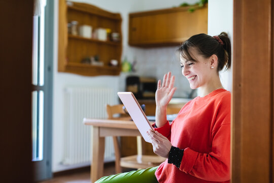 Smiling woman waving hand to video call on digital tablet at home