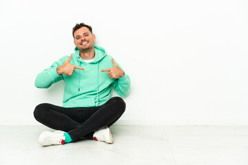 Obraz premium Young handsome caucasian man sitting on the floor proud and self-satisfied