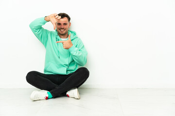 Fototapeta premium Young handsome caucasian man sitting on the floor focusing face. Framing symbol