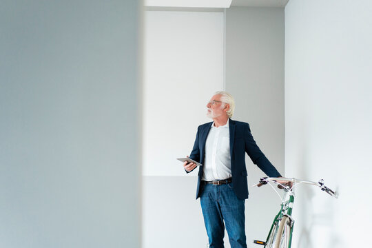 Senior male professional looking away while standing near bicycle at office