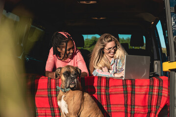 Multiracial people with dog traveling together retro mini van transport - Digital nomad concept working at laptop computer - Focus on african girl face