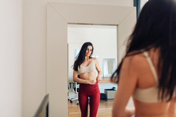 Woman looking in mirror while adjusting pants in living room at home