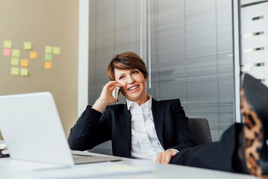 Happy businesswoman looking away while talking on smart phone at desk