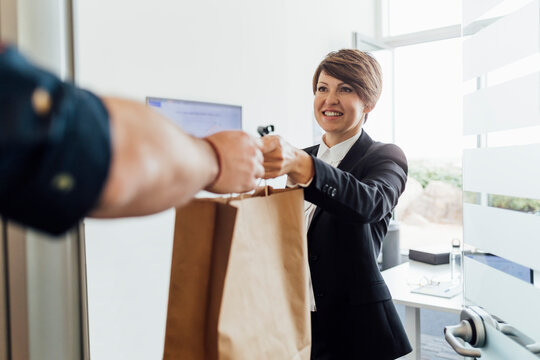 Smiling Female Entrepreneur Receiving Food Bag From Delivery Person At Office