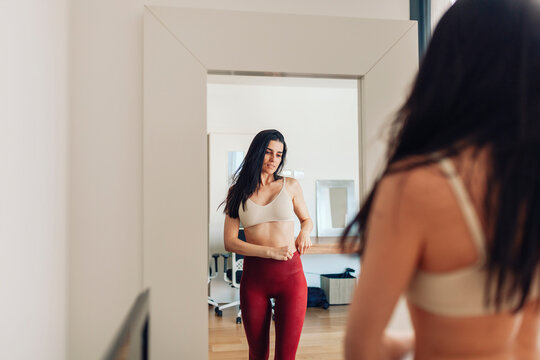 Woman Looking In Mirror While Adjusting Pants In Living Room At Home