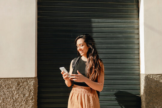 Smiling female tourist using smart phone while standing in front of shutter