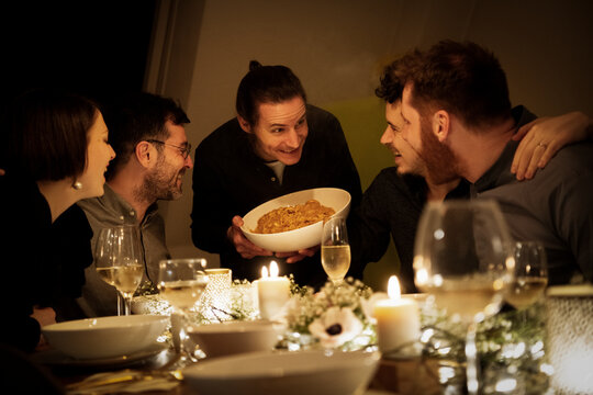 Smiling man offering pasta to male and female friends at home