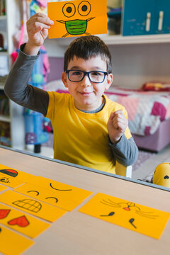 Boy with eyeglasses holding emoticon above head while playing at home